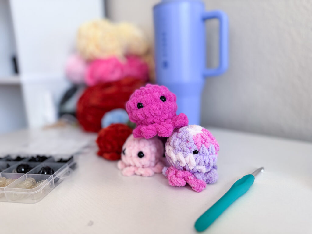 Stack of three mini crochet octopus plushies on a desk with a crochet hook